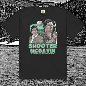 Puede incluir: Camiseta negra con un gráfico de dos hombres, una pelota de golf y el texto "SHOOTER MCGAVIN". El texto "I EAT PIECES OF SH*T LIKE YOU FOR BREAKFAST" está debajo. El diseño utiliza colores verdes, blancos y beige.