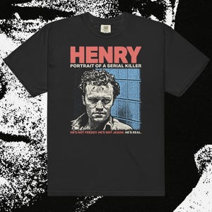 May include: Black t-shirt featuring the text "HENRY PORTRAIT OF A SERIAL KILLER" in red and a black and white portrait of a man. Below the portrait, the text reads "HE'S NOT FREDDY. HE'S NOT JASON. HE'S REAL."