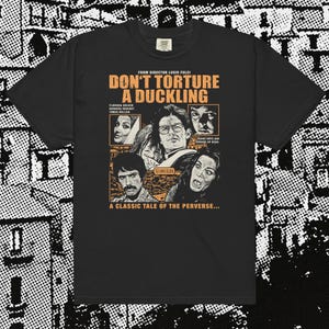 Op de afbeelding: Zwart T-shirt met een filmposterontwerp voor "Don't Torture a Duckling". Het ontwerp bevat oranje tekst en afbeeldingen van acteurs. Het shirt bevat de tekst "A Classic Tale of the Perverse..."