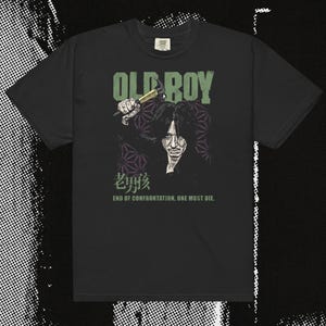 May include: Black t-shirt featuring a graphic from the film "Oldboy." The design includes the text "OLD BOY" in green, a stylized illustration of a man, and Japanese text. The phrase "END OF CONFRONTATION, ONE MUST DIE" is also included.