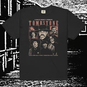May include: Black t-shirt featuring a graphic from the film "Tombstone." The design includes the film's title, cast portraits, and the text "A Film by George P. Cosmatos" and "Every town has a story, Tombstone has a legend."