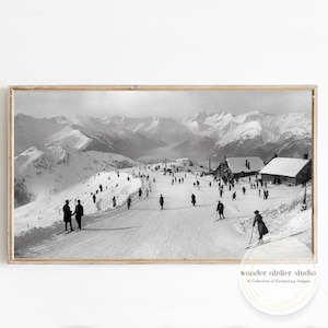 Könnte beinhalten: Schwarz-Weiß-Druck in einem Rahmen einer Vintage-Skisport-Szene. Das Bild zeigt Skifahrer auf einer schneebedeckten Piste mit Berggipfeln im Hintergrund. Mehrere Gebäude sind sichtbar, und die Gesamtästhetik erinnert an ein klassisches Foto.