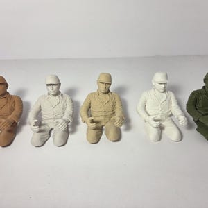 Puede incluir: Cinco figuras en miniatura de figuras sentadas que llevan sombreros y uniformes de trabajo. Las figuras son de varios colores, incluyendo marrón, blanco roto, beige y verde oliva. Las figuras posan con las manos apoyadas en su regazo.