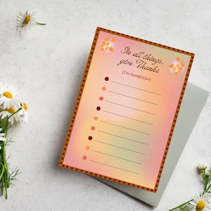 May include: A rectangular, gradient-colored card with the text "In all things, give Thanks" and lines for writing. The card has a decorative border and is accompanied by a gray envelope and daisies.