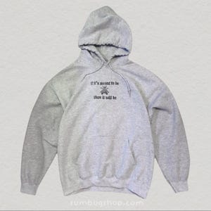 May include: A heather gray hoodie with a drawstring hood and a front pocket. The hoodie features the embroidered text "if it's meant to be then it will be" above a small insect graphic. The website "sumbugshop.com" is printed at the bottom.