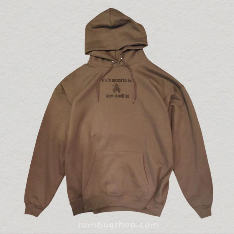 May include: A brown hoodie with a drawstring hood and a kangaroo pocket. The front of the hoodie features the text "If it's meant to be then it will be" in a dark color. The website address "sumbugshop.com" is at the bottom.