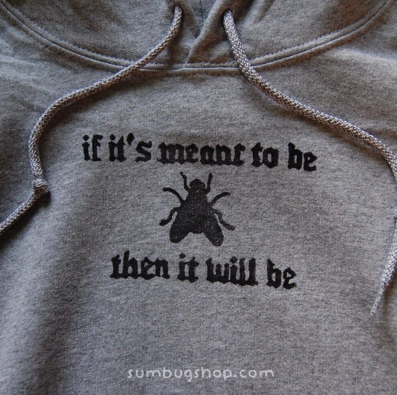 May include: A gray hooded sweatshirt with a drawstring. The front features the phrase "if it's meant to be then it will be" in black gothic lettering, with a black fly graphic. The website address sumbugshop.com is at the bottom.