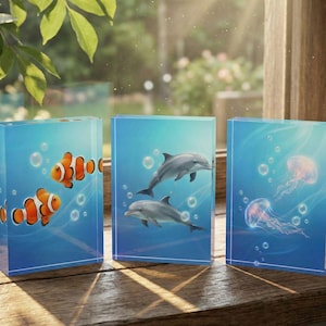 May include: Three rectangular decorative blocks with underwater scenes. One block features clownfish, another dolphins, and the third jellyfish. The blocks are blue with white bubbles and are displayed on a wooden surface.