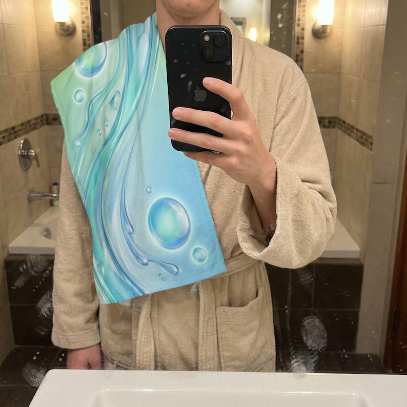 May include: A blue and green bath towel with a water-themed design. The towel features a swirling pattern of blue and green with bubbles and water droplets. The towel is made of a soft material.
