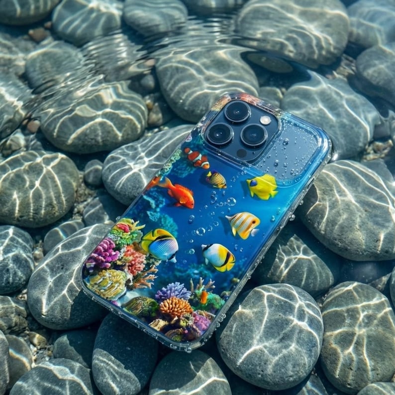 Pode incluir: Capa de telefone transparente com um design subaqu&aacute;tico vibrante. Apresenta peixes coloridos e corais. A capa est&aacute; na &aacute;gua, sobre pedras cinzentas. Os peixes s&atilde;o laranja, amarelos e azuis.