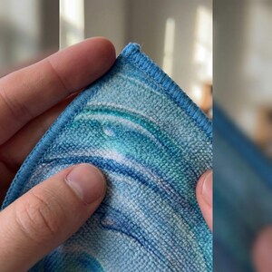 May include: Close-up of a microfiber cleaning cloth with a blue and white swirl pattern. The cloth has a stitched blue border. The texture of the cloth is visible, highlighting its absorbent qualities. Ideal for cleaning.