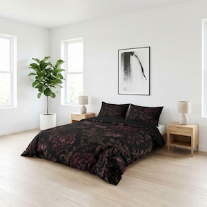 May include: A bedding set featuring a black duvet cover and two matching pillowcases with a dark purple and black floral damask pattern. The bedding is arranged on a bed frame with two light wood nightstands and matching table lamps.