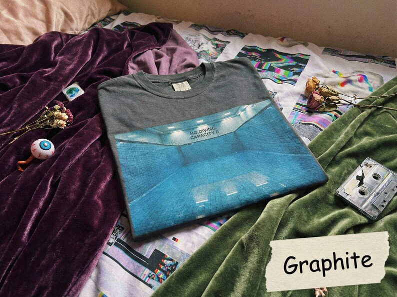 May include: A graphite gray t-shirt with a blue and white graphic of a pool interior. The shirt has the text "NO DIVING CAPACITY 0" on the graphic. The word "Graphite" is written on a white label.
