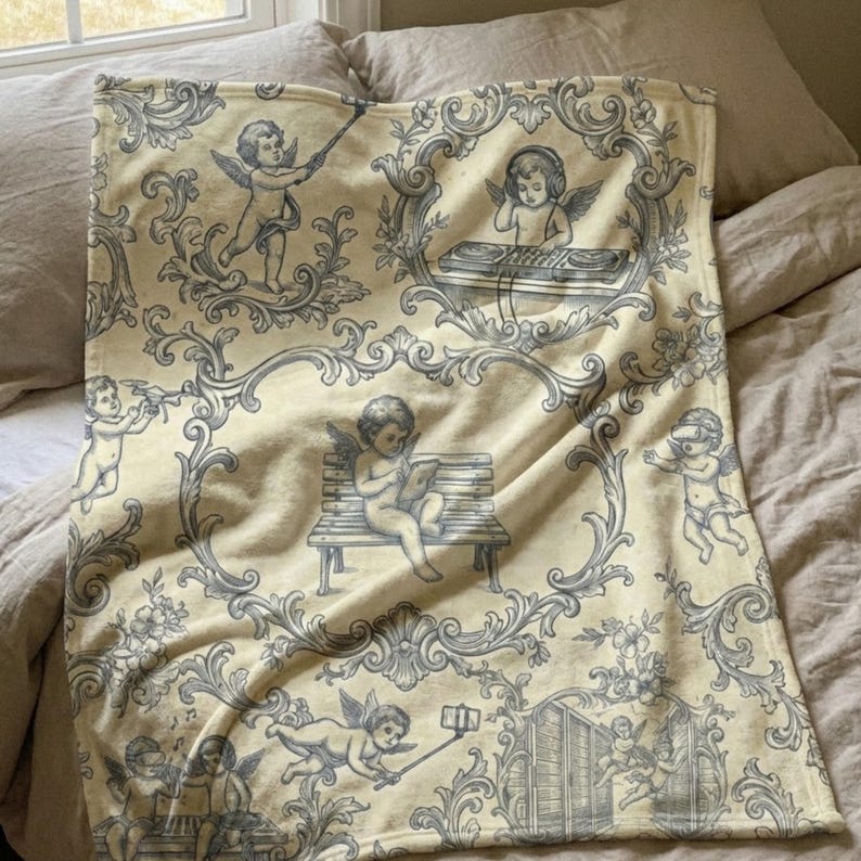 May include: A cream-colored blanket featuring a repeating pattern of cherubs in various poses, framed by ornate gray scrollwork. The cherubs are depicted with wings, some using a selfie stick, reading, or listening to music. The blanket is folded on a bed.