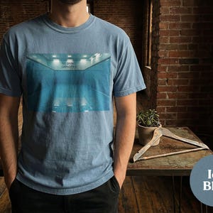 May include: Ice blue t-shirt featuring a graphic of a blue indoor pool with the text "NO DIVING CAPACITY 0". The shirt is a solid color and has a crew neck.