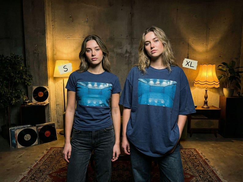 May include: Two navy blue t-shirts, one size S and one XL, featuring a blue graphic design. The shirts are worn by two people in a room with vintage decor, including a rug, lamps, and vinyl records.