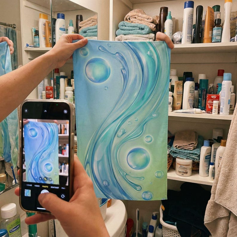May include: A blue and green abstract painting with flowing water and bubbles. The artwork is held up in a bathroom setting, with a phone capturing the image. The painting features a gradient of colors.