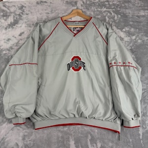 May include: A light gray V-neck pullover windbreaker jacket featuring red piping accents. The center chest displays the Ohio State logo in red, white, and black, while the word KEYES is embroidered in red on the right sleeve.