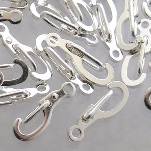 May include: A close-up of a pile of silver-toned metal lobster claw clasps. The clasps are small and have a shiny finish.