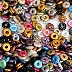 May include: A large assortment of colorful, iridescent, and metallic donut-shaped beads. The beads are made of glass and have a smooth, shiny finish. They are perfect for jewelry making, crafts, and other creative projects.