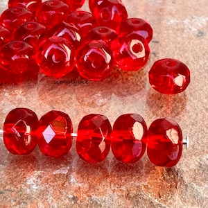 May include: A strand of red glass beads with a faceted finish. The beads are strung on a silver wire.