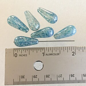 K&ouml;nnte beinhalten: Sechs blau-wei&szlig; tropfenf&ouml;rmige Glasperlen. Die Perlen sind etwa 2,5 cm lang. Ein Metallstift ist durch eine Perle gesteckt. Ein Lineal mit Zollma&szlig;en befindet sich im Vordergrund.