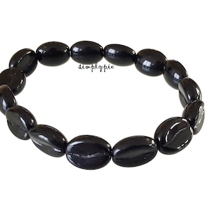 May include: A black beaded bracelet with oval-shaped beads. The beads are strung together to form a circular shape. The bracelet is on a white background. The text "simplypie" is visible on the image.