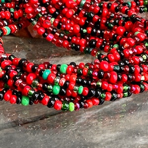 May include: A close-up of a multi-strand beaded necklace with red, black, green, and silver beads. The beads are small and round, and the necklace is coiled up.