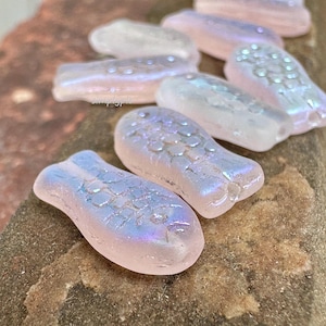 May include: A collection of iridescent pink glass fish charms with a textured surface. The fish have a light blue iridescent sheen.