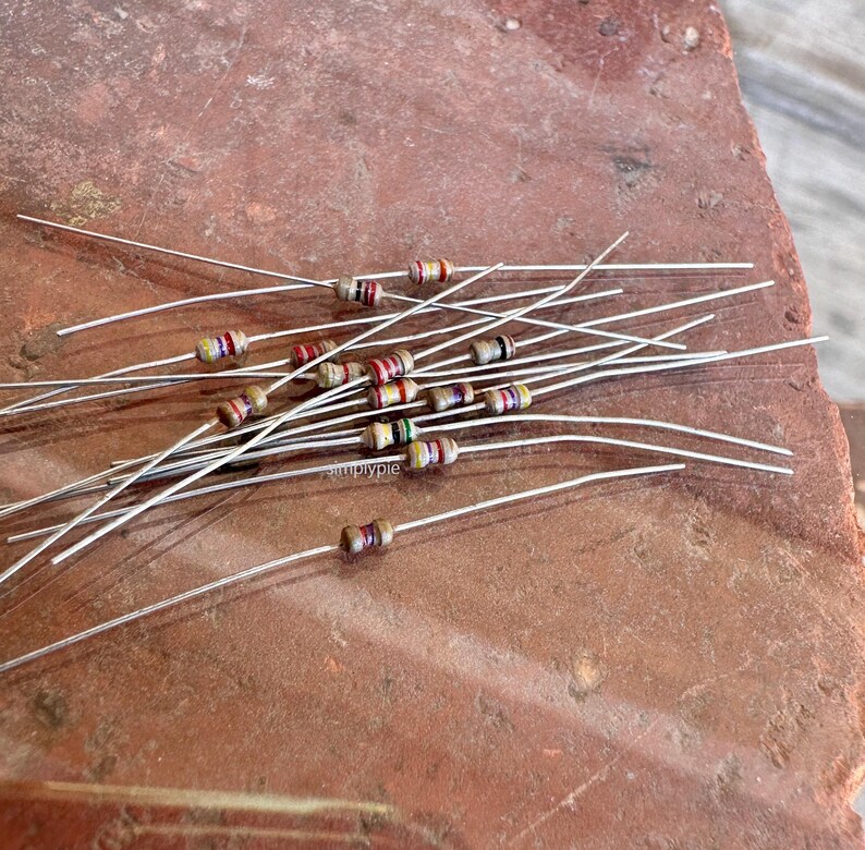 Puede incluir: Una colecci&oacute;n de peque&ntilde;as resistencias electr&oacute;nicas con cuerpos cil&iacute;ndricos que presentan bandas de colores. Cada resistencia tiene dos cables met&aacute;licos largos, delgados y rectos que se extienden desde los extremos opuestos.