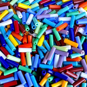 May include: A large assortment of colorful glass beads in various shades of blue, green, red, yellow, and purple. The beads are all cylindrical in shape and have a smooth, glossy finish.