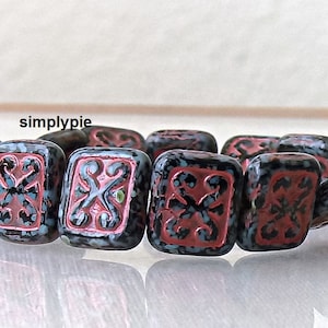 May include: A strand of black and red square glass beads with a decorative pattern. The beads have a speckled finish and are strung together on a clear thread.