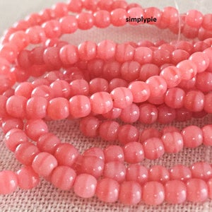 Peut inclure: Un brin de perles de verre roses avec un motif rayé. Les perles sont petites et rondes, et elles sont enfilées sur un fil transparent.
