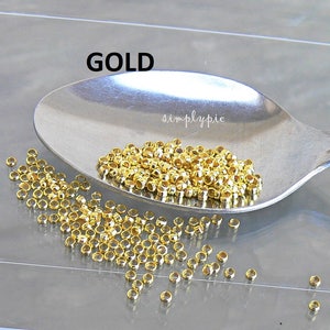 Puede incluir: Una cuchara llena de anillas de salto de metal de color dorado. Las anillas de salto son peque&ntilde;as y redondas, y est&aacute;n dispersas sobre una superficie blanca.