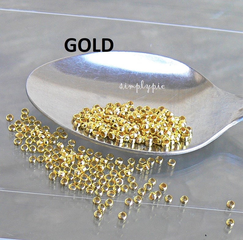 Puede incluir: Una cuchara llena de anillas de salto de metal de color dorado. Las anillas de salto son peque&ntilde;as y redondas, y est&aacute;n dispersas sobre una superficie blanca.