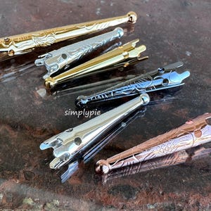 May include: Five different metal knitting needle tips with decorative designs. The tips are gold, silver, black, and copper.