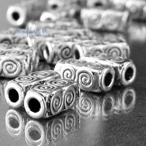 Peut inclure: Gros plan sur des perles en m&eacute;tal argent&eacute; avec un motif en spirale. Les perles sont dispos&eacute;es en rang&eacute;e et r&eacute;fl&eacute;chissent la lumi&egrave;re.