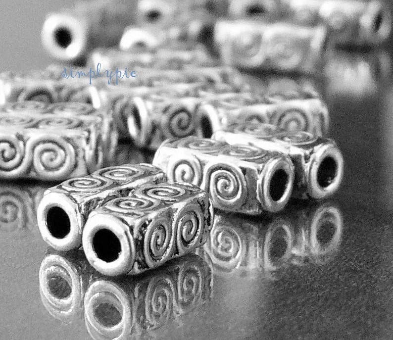 Peut inclure: Gros plan sur des perles en m&eacute;tal argent&eacute; avec un motif en spirale. Les perles sont dispos&eacute;es en rang&eacute;e et r&eacute;fl&eacute;chissent la lumi&egrave;re.