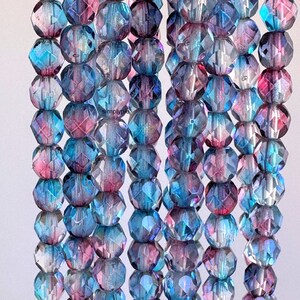 May include: A strand of faceted glass beads in shades of blue and pink. The beads are iridescent and have a slightly cloudy appearance.