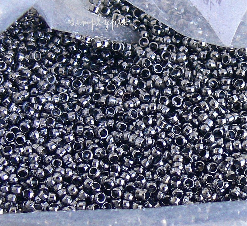 Puede incluir: Una vista de cerca de una gran cantidad de peque&ntilde;as cuentas redondas de metal de color plateado. Las cuentas est&aacute;n dispuestas en un patr&oacute;n aleatorio y parecen estar en una bolsa de pl&aacute;stico.