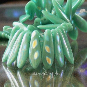 May include: A strand of iridescent green glass beads with gold flecks. The beads are shaped like teardrops and are strung on a clear thread.