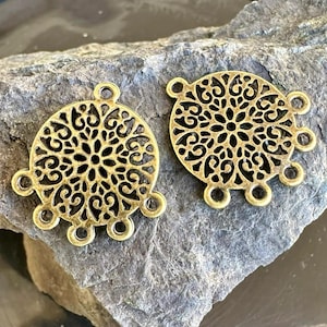 May include: Two circular antique gold-toned metal jewelry connectors featuring an intricate openwork filigree pattern. Each round component has multiple small loops extending from the outer edge for attaching additional jewelry elements.