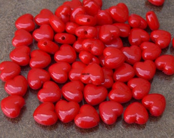 May include: A collection of glossy, heart-shaped beads in a vibrant red hue. These small beads have a smooth, reflective surface and a hole for stringing. Ideal for jewelry making or craft projects.