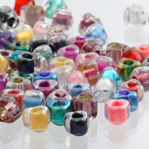 May include: A collection of colorful glass beads in various shapes and sizes. The beads are mostly transparent with some having iridescent finishes. The beads are scattered on a white surface.