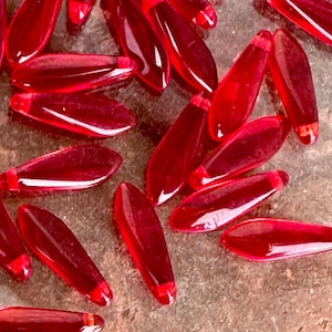 May include: A collection of red glass teardrop-shaped beads. The beads are translucent and have a glossy finish.