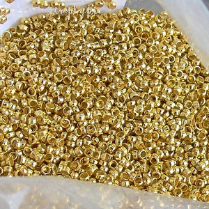Puede incluir: Una gran cantidad de cuentas de metal de color dorado. Las cuentas son peque&ntilde;as y redondas, con un agujero en el centro. Est&aacute;n dispuestas en una pila, y la imagen se toma desde una perspectiva cercana.