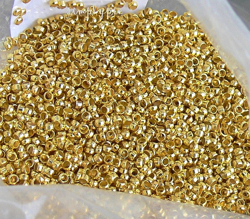 Puede incluir: Una gran cantidad de cuentas de metal de color dorado. Las cuentas son peque&ntilde;as y redondas, con un agujero en el centro. Est&aacute;n dispuestas en una pila, y la imagen se toma desde una perspectiva cercana.