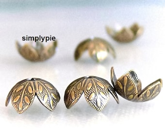 May include: Six antique gold-toned metal bead caps with a leaf design. The caps are open on one side and have a small hole in the center.
