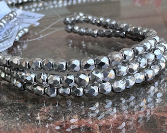 May include: A strand of metallic silver-colored beads with a faceted, multi-sided surface texture. The beads are strung together on a thin, clear filament, creating a continuous loop of reflective, uniform spherical shapes with a polished finish.