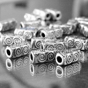 Peut inclure: Gros plan sur des perles en m&eacute;tal argent&eacute; avec un motif en spirale. Les perles sont cylindriques et ont une finition lisse et polie.